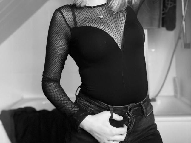 Scarlet-Young-hot wears a black mesh long-sleeve top with a deep V-neck, showing her tits, and dark jeans with her hand on her crotch. Black-and-white photo.