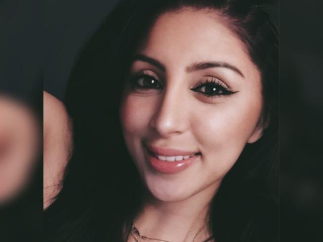 RaquelZ has smooth, dark brown hair, full lips with pink gloss, and thick, black eyeliner. Her cute smile shows white teeth. She's attractive with light brown skin.