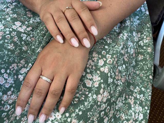 Mirellias Hände mit rosafarbenen Nägeln, die eine Hand trägt einen goldenen Ring mit einem Diamanten und die andere eine schmale goldene Band, ruhen auf einem grünen Kleid mit Blumenmuster..