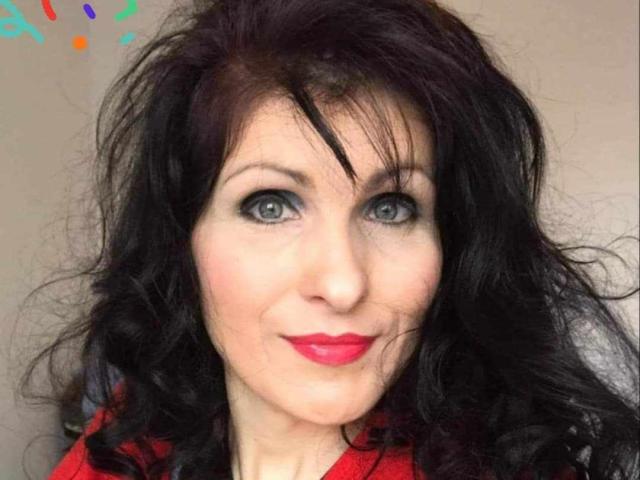 BettyLoveHot has wavy black hair, blue eyes, and red lipstick. She's smiling with a cute, slightly wrinkled face, wearing a red shirt. Her tits are not visible.