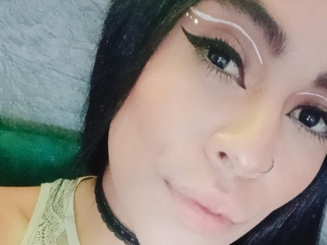StellaBeckker has dark hair, a nose ring, and white eyeliner wings. She's wearing a black choker and a lace top, with a soft, slight smile.