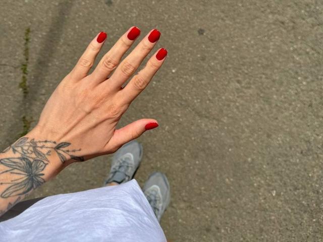 La mano de Zuckerberg, con uñas rojas, mostrando un tatuaje de una mariposa, sobre un pavimento gris. Se pueden ver los pantalones cortos blancos y las zapatillas grises de Zuckerberg en la parte inferior..
