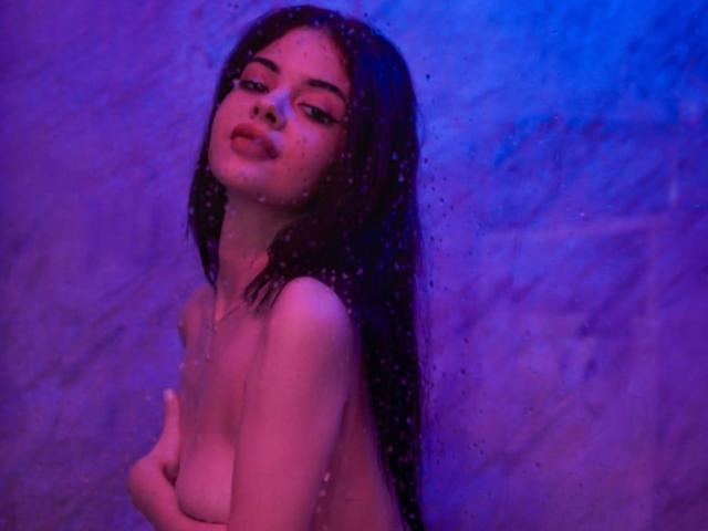 MolyStar with long dark hair, naked, blue-purple light, covering small tits with hands, wet from water droplets, slightly open mouth, looking up, soft expression.
