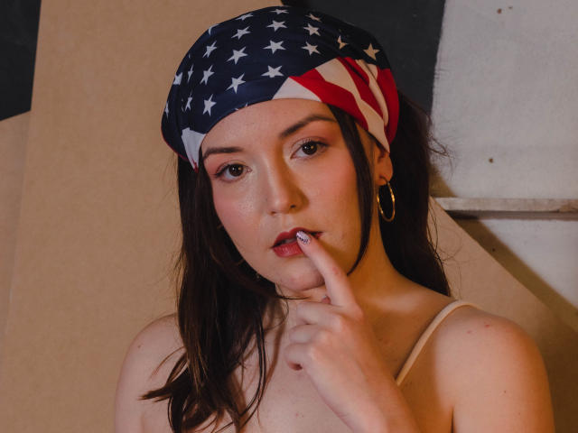 Topless MollyMarmalade with an American flag bandana, finger to lips, showing off her tits, has brown hair, hoop earrings, and a cute, slightly freckled face.