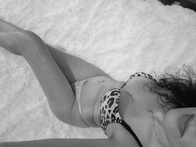 AddictedToUTS is lying on a fluffy white rug, wearing a leopard print bra and lace panties, with her legs slightly apart, showing her belly button and a necklace.