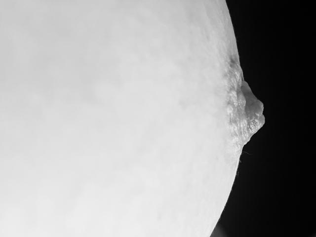 A grayscale image of a moon with a rough, rocky edge on the right side, showing detailed texture and shadows against a black background.