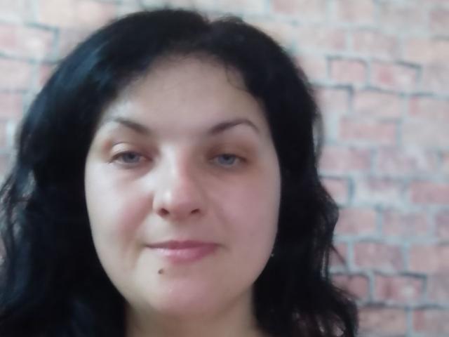 TaisiawSolo has black wavy hair, light skin, blue eyes, and a small black mole under her right lip. She's smiling slightly. Her tits are not visible.