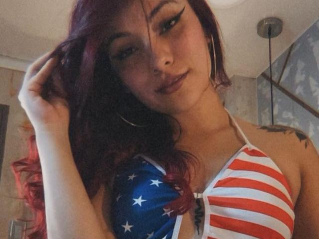 ValeryHarllow with red hair, wearing a striped American flag swimsuit, showing her tits and ass, holding her hair, with a tattoo on her side.