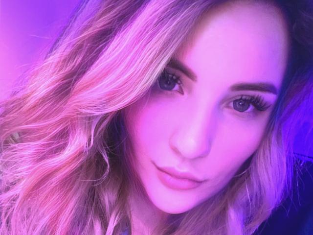 AnitaXRouses a les cheveux blonds ondulés, d'une couleur rose-violette, des yeux bleus et un visage piquant avec des lèvres pulpeuses. Son maquillage comprend de longs cils. Elle regarde légèrement sur le côté..