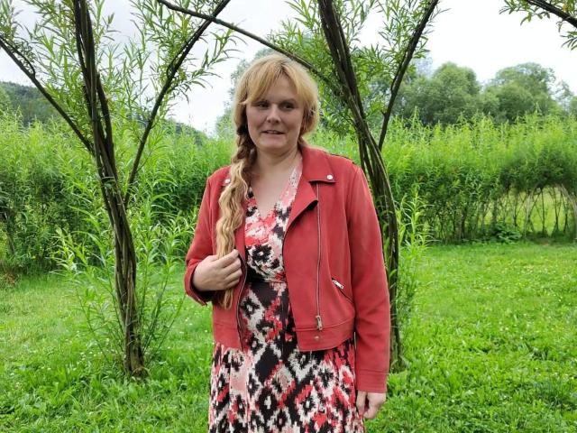 BeaLust-hot with long blonde hair, red jacket, and patterned dress stands in a green field, holding her jacket's zipper. Her tits are small, and she's smiling slightly.