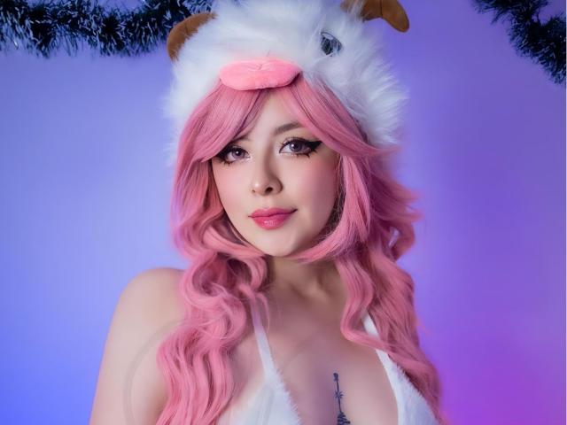 NeeKolombiana with pink wavy hair, white furry hat with brown horns, and pink nose, wearing a white fur bikini, has cute makeup and a small tattoo below her tits.