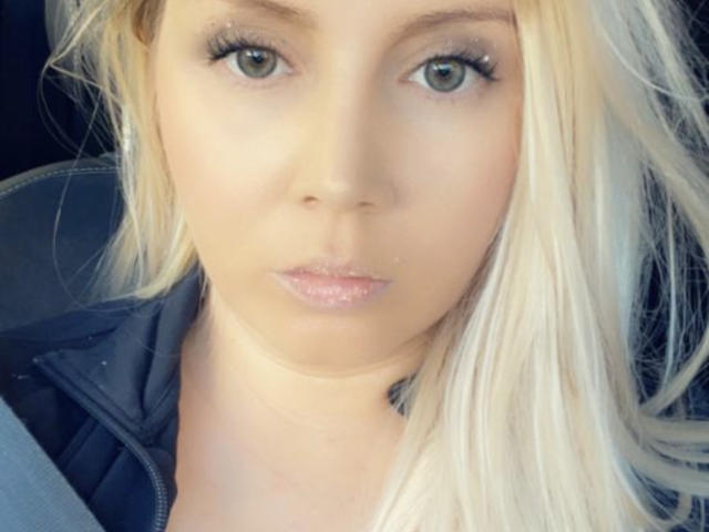 SarrahXHot has blonde hair, green eyes, and slightly pouty pink lips. She's wearing a black jacket with a zipper. Her face is centered in the image.