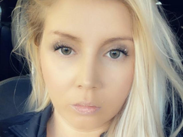SarrahXHot has blonde hair, green eyes, and full pink lips with a slightly pouty expression. She's looking straight at the camera with a serious, sexy face.
