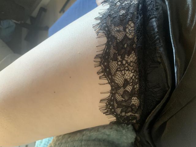 SharonStorm's pale thigh with black lace lingerie and leather skirt, showing intricate lace patterns and frayed edges, in a soft, natural light.