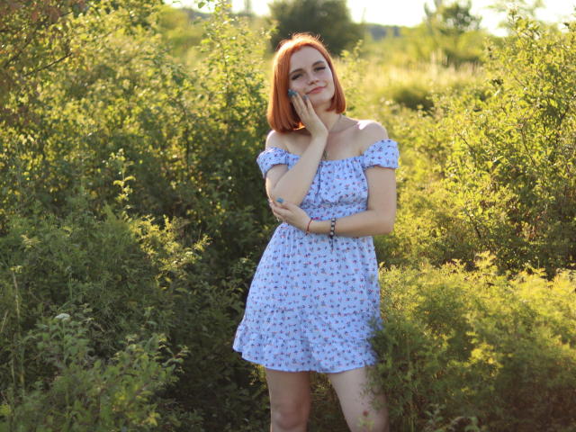 MargaritaKis with red hair, white off-shoulder dress, small tits, standing in green bush, hand on cheek, smiling, sunlight, summer, bracelet on wrist.