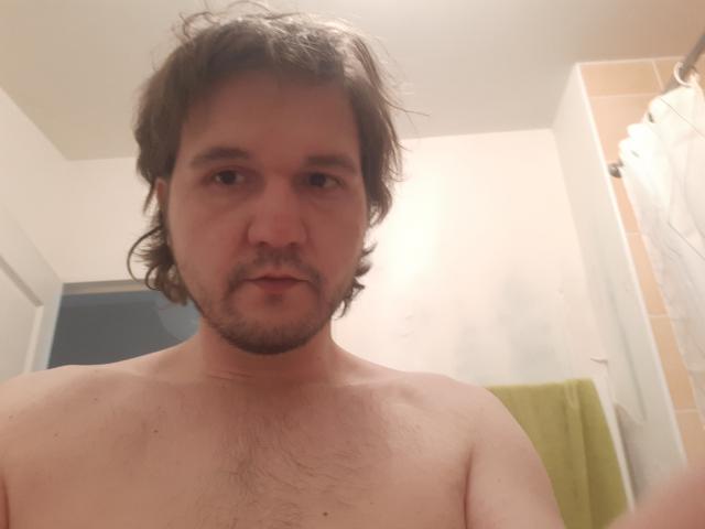 NectarineFad, shirtless with wavy brown hair, light beard, and chest hair, looking into the camera with a neutral expression.