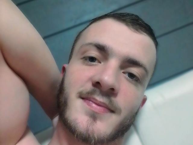 Vrrr has a short brown beard, slight mustache, and is smiling with his arm raised. His head is close to the camera, showing a relaxed expression.