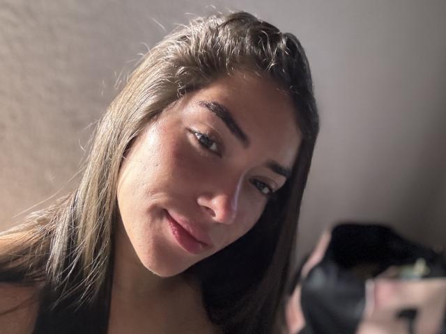 SharonKlart with wet brown hair, slightly tilted head, and subtle smile, showing her face and small nose in a soft light. She has small tits and dark eyebrows.