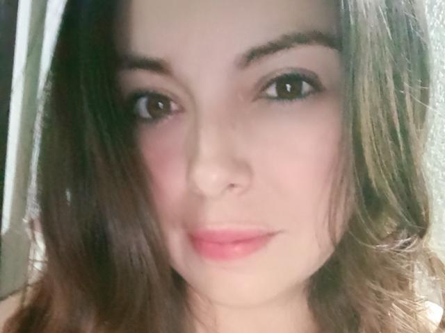 O rosto de Seher, com olhos castanhos, um leve sorriso, lábios rosados, pele clara, cabelos castanhos ondulados e maquiagem discreta. Ela tem um nariz delicado e olha diretamente para a câmera..