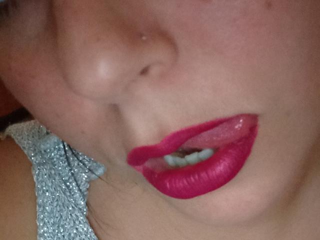 BiaSexy69's face, showing a nose with a small boogers, and glossy pink lips slightly parted, wearing sparkly silver top, close-up shot, with visible teeth.