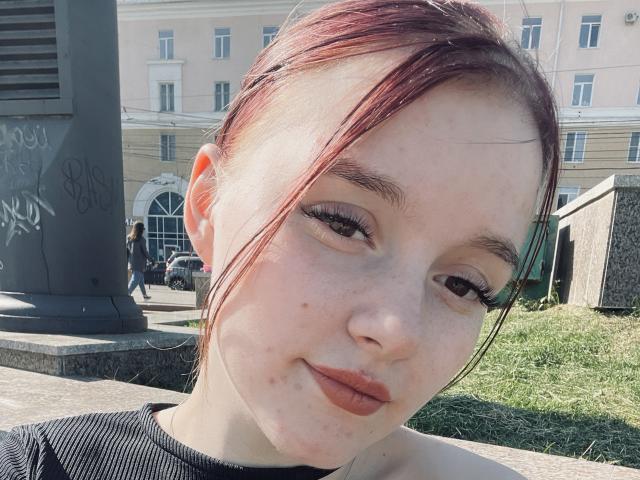 DaMa69s a une peau pâle, des cheveux roux-brun attachés en un chignon désordonné, et porte un eye-liner noir avec de longs cils. Elle sourit légèrement, laissant entrevoir ses lèvres brunes. Elle porte un haut noir..