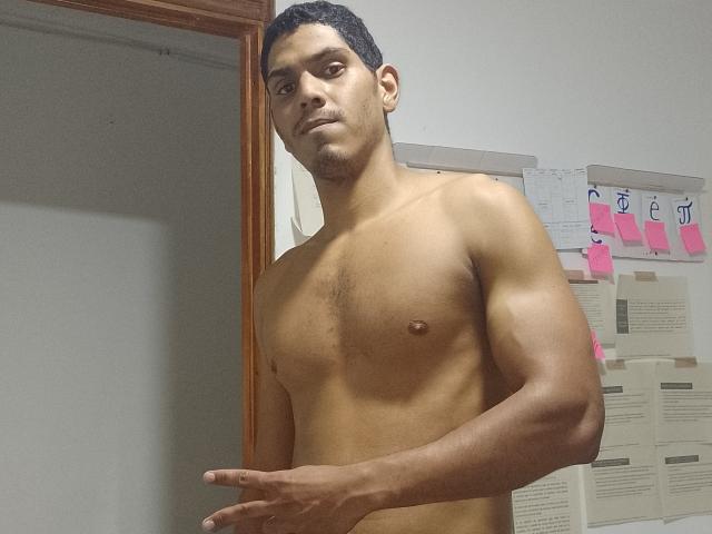 McBride is a shirtless, muscular, dark-skinned guy with short curly hair, standing in a room, pointing with his right hand, and looking slightly to the side.