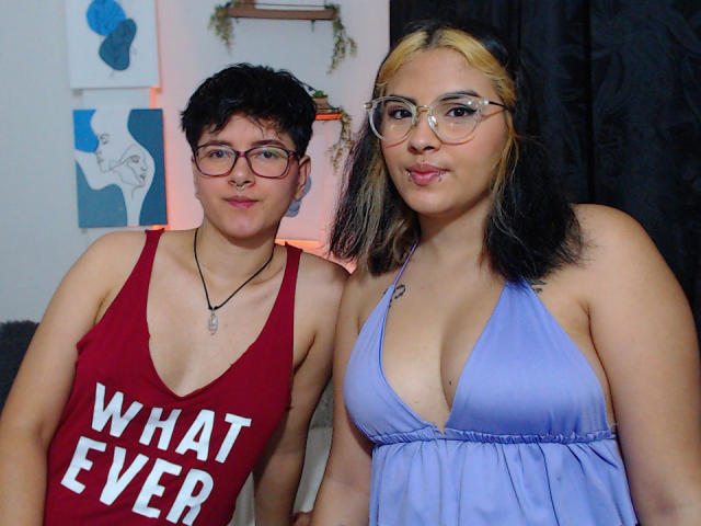 Twee vrouwen met een bril, CamilleAndSophie links in een rood tanktop met de tekst "WHAT EVER" en Sophie rechts in een paars topje met halter, waarbij haar borsten zichtbaar zijn..
