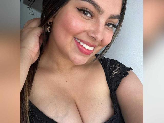 HoneyBoo with a smile, brown eyes, and nose ring, wearing a black lace top, showing her big tits, brown hair in a braid, and pink lipstick.