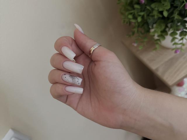 SugarrX's hand with long, white, pointed nails, a silver ring, and a white nail with black dots. Her skin is fair, and she's holding her hand up.