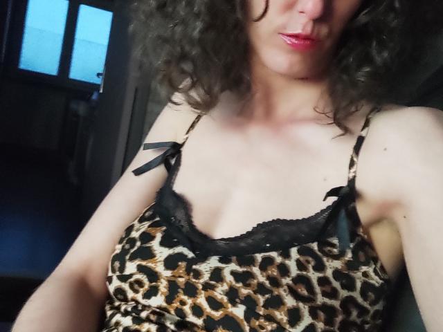 NinaAndGreg with curly brown hair, pink lipstick, wearing a leopard print camisole with black lace trim and ribbons, showing small tits and a slight tan.
