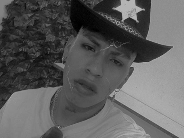 SebastianLeeymond with a cracked face, wearing a police hat, white shirt, and chain, looking tired with a small earring in his left ear. Black and white image.