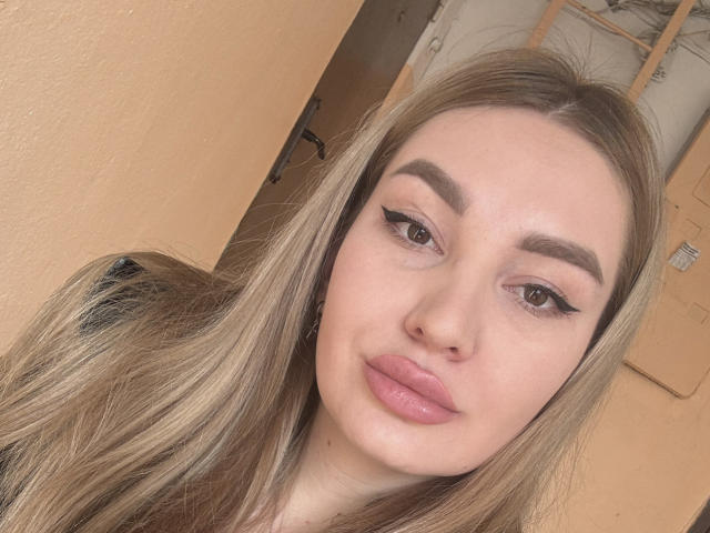 EvaIce69 has long blonde hair, thick eyebrows, pink eyeliner, and pink lipstick, with a nose piercing and a slight smile, looking directly at the camera.