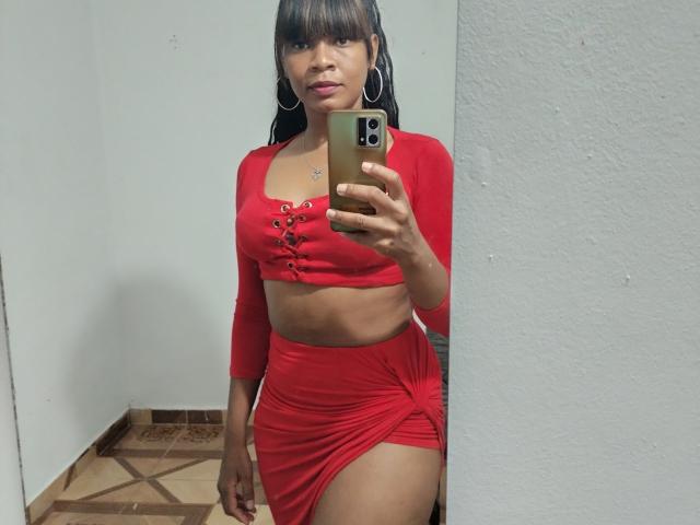 Haddie with dark hair in a red crop top and matching skirt, holding a phone in a mirror selfie, showing her ass and midriff. Wearing hoop earrings.