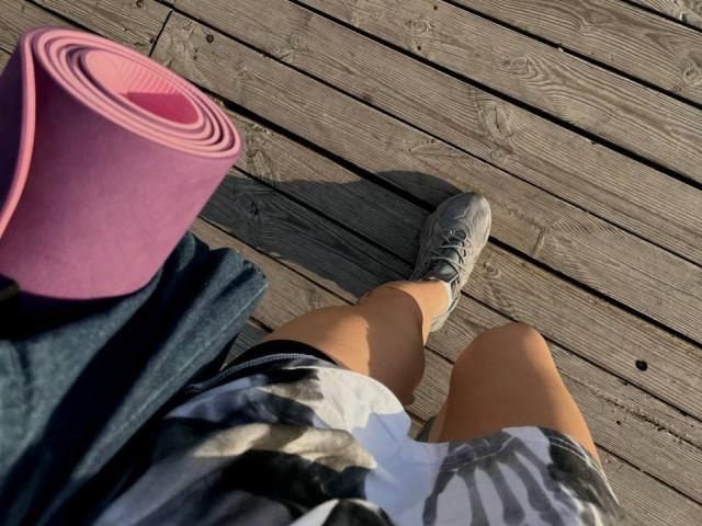 Tsukerberg's legs in plaid shorts, white sneakers, with a pink yoga mat and blue jacket on wooden floor, shot from above.