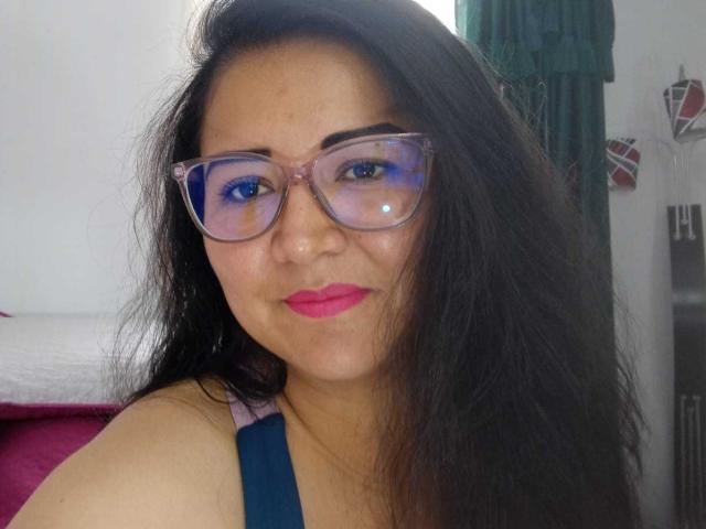 Philipa has long black hair, wears clear glasses with blue reflections, and pink lipstick. She's looking at the camera with a slight smile, wearing a blue top.