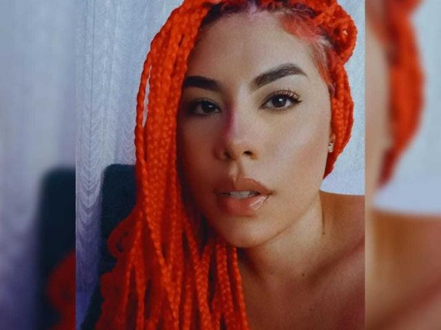 lilsWay with bright orange, crocheted dreadlocks, full lips, and dark eyebrows, staring into the camera, showing off her cute nose and subtle makeup.