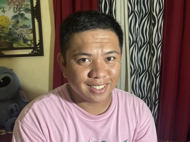 OneSpiceDiva, short black hair, medium skin, slight smile, wearing pink shirt, visible sweat on face, medium build, sitting, zebra-patterned and red curtains in background.