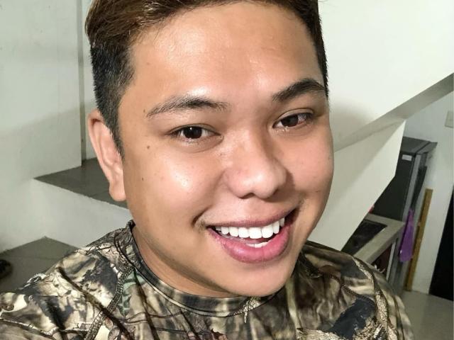 OneSpiceDiva has short brown hair, tan skin, and a smiling face with white teeth. She's wearing a camouflage shirt, and her brown eyes are looking at the camera.