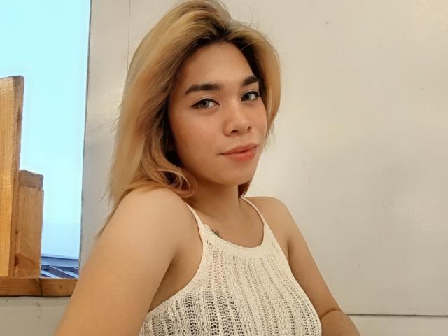 Godin Hera met blond haar, een witte gebreide top, kleine borsten en lichte huid, die in de camera kijkt met een lichte glimlach, zachte make-up en subtiele eyeliner..