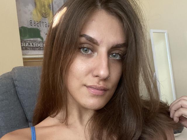 Kametia, avec ses longs cheveux bruns, ses yeux verts et son anneau de nez, se tient la chevelure, révélant ainsi son visage légèrement rougi et sa robe à bretelles bleues. Ses seins sont petits, et elle est mignonne..