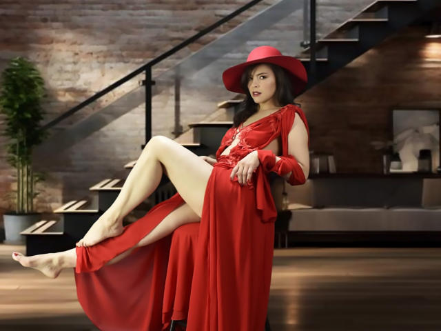 Scottie, vêtue d'une robe et d'un chapeau rouges, est assise avec une jambe levée, montrant ses fesses nues et sa peau pâle. Elle a les cheveux foncés et un regard séduisant..