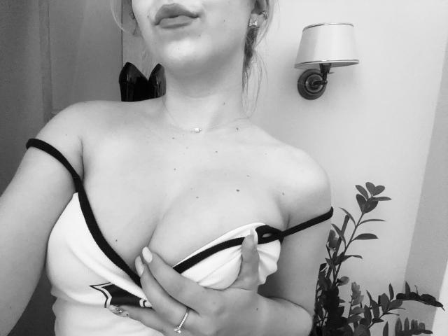 SugarrX, mit hochgezogenen Brüsten, in einem trägerlosen Top, die ihre großen Brüste hält, ihr Dekolleté zeigt und ein leichtes Lächeln hat, in einem Schwarz-Weiß-Selfie..