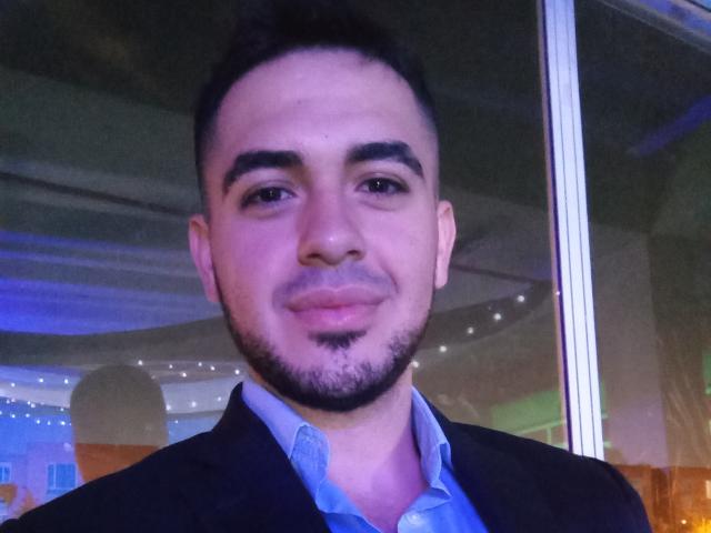 Elruglis69 has a medium skin tone, short black hair, dark eyebrows, a small goatee, and a slight smile. He's wearing a black suit with a blue shirt.