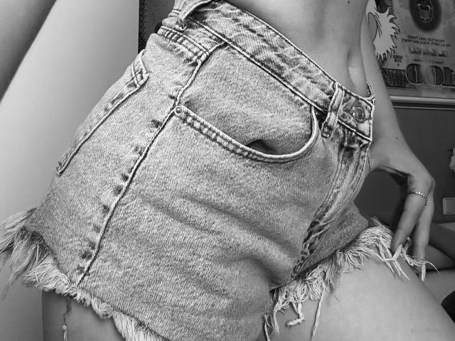 SugarrX's frayed denim shorts, showing a tight butt and small back pocket, with a ring on their left hand, in a black and white photo.