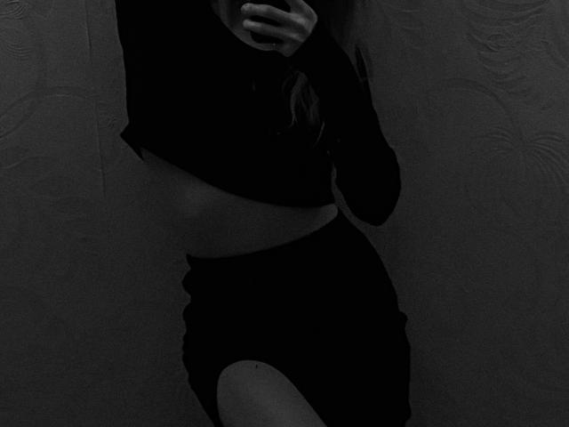 AlexSantorski's dark, tight, long-sleeve top reveals a flat, toned midriff, and she's wearing black, high-waisted pants with a cutout on the left thigh. She's holding a phone.