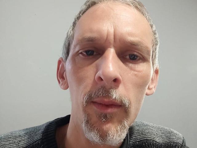 FreyDudu has a balding head with gray hair, a small mustache, and a goatee, wearing a gray sweater, looking slightly confused with a neutral expression.