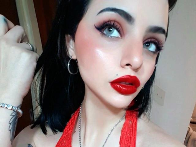 Celestia-hot with glossy red lips, black eyeliner, and hoop earrings, looking up with blue eyes. She's wearing a red lace halter and a diamond bracelet.