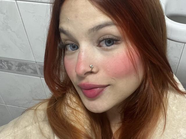 ShantalSummer tiene cabello rojo, ojos azules, mejillas rosadas y un piercing en la nariz. Lleva lápiz labial rosa y una blusa blanca, y en la foto no se ve su trasero..