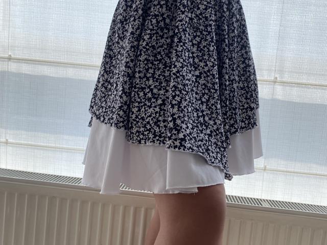 Mirellia's floral skirt with a white underskirt, showing her bare thighs. The skirt is blue with small white flowers, and the photo is taken from behind.