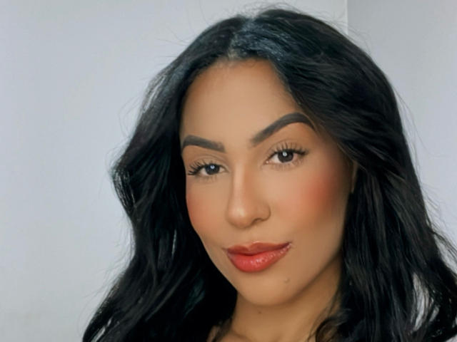 EllenS69 has black wavy hair, thick eyebrows, red lipstick, and a subtle smile. Her brown skin has a smooth, even tone. She looks attractive and confident.